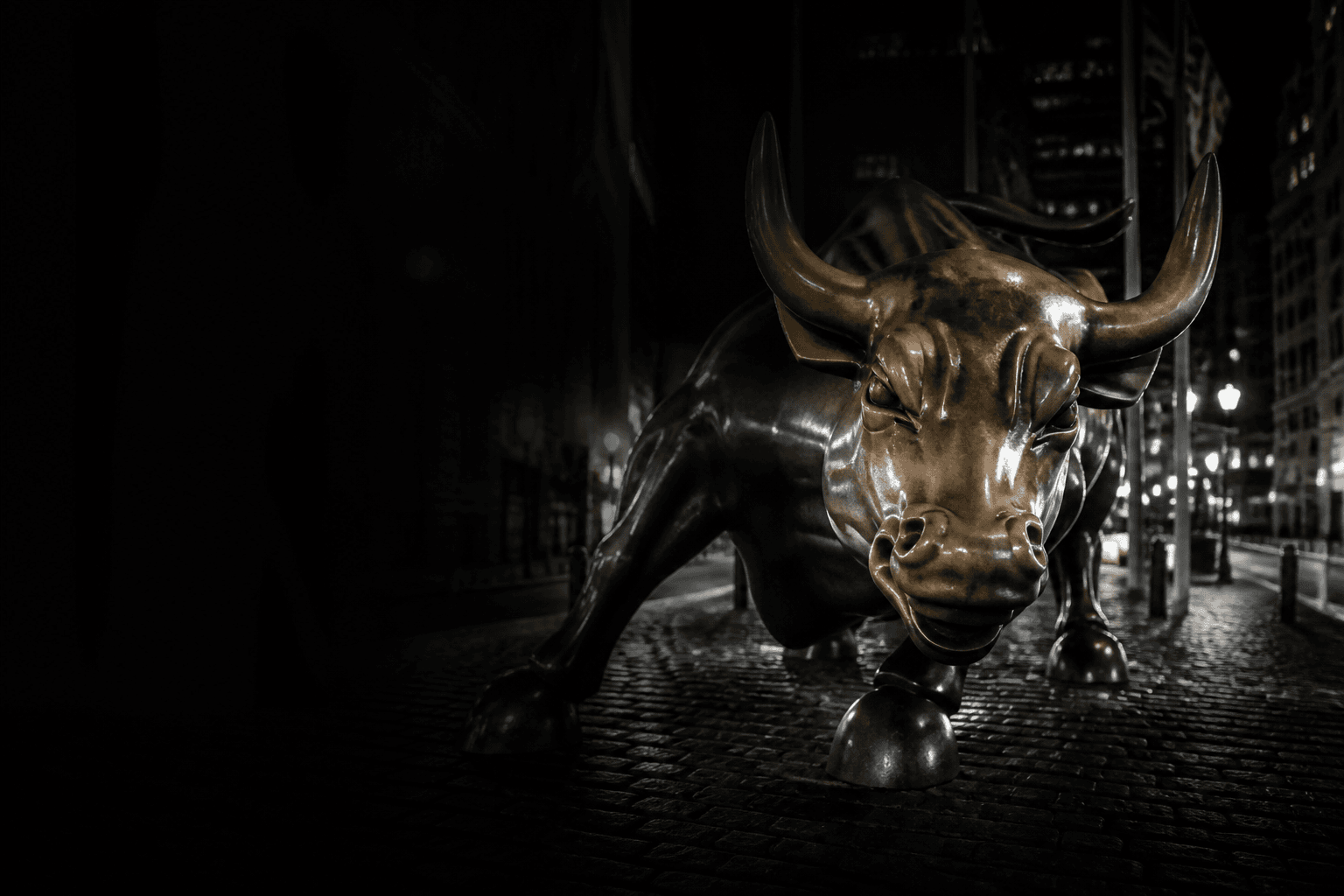 Charging bull statue in a financial district at night