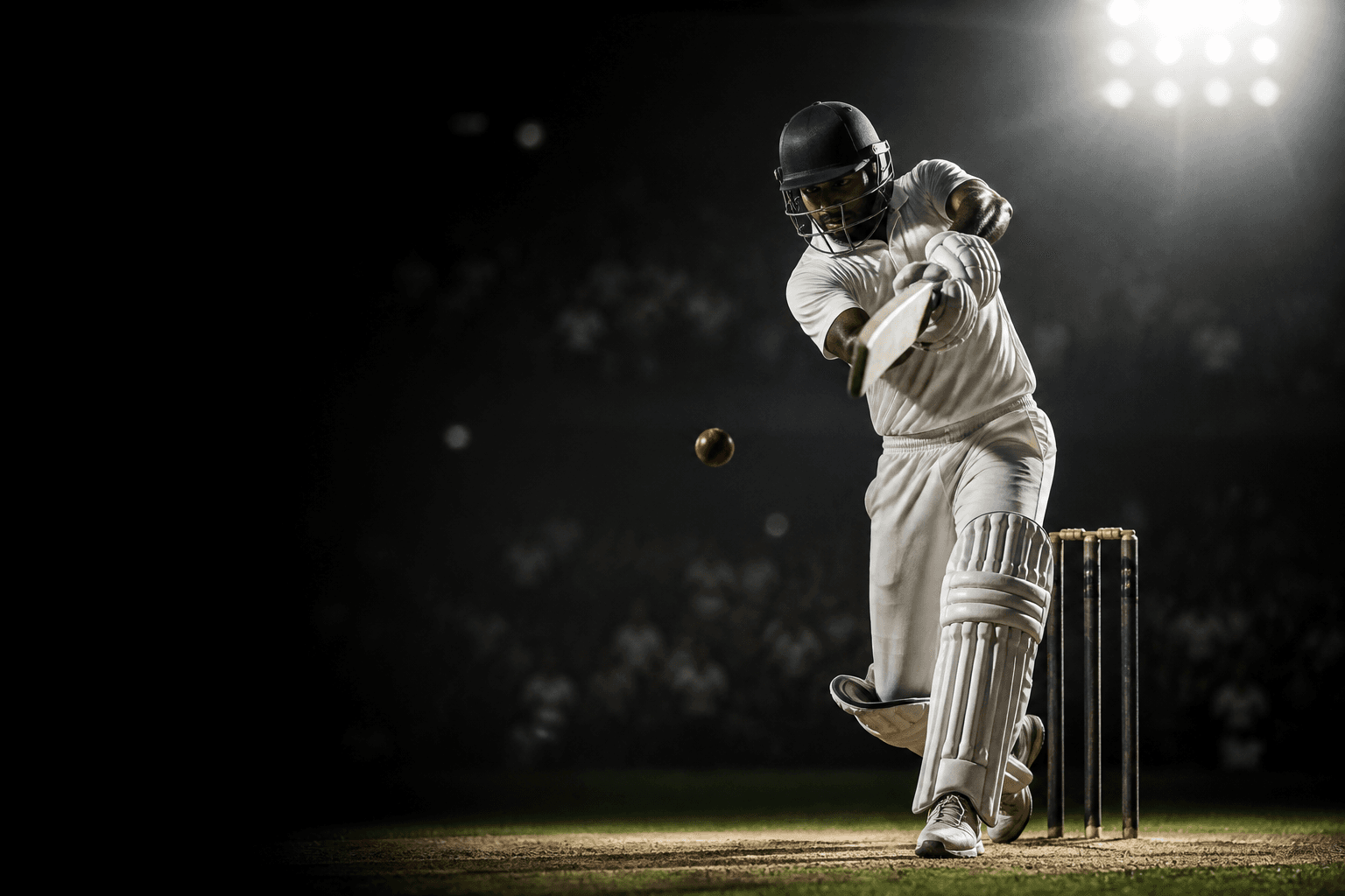 Cricketer playing a batting shot under stadium lights